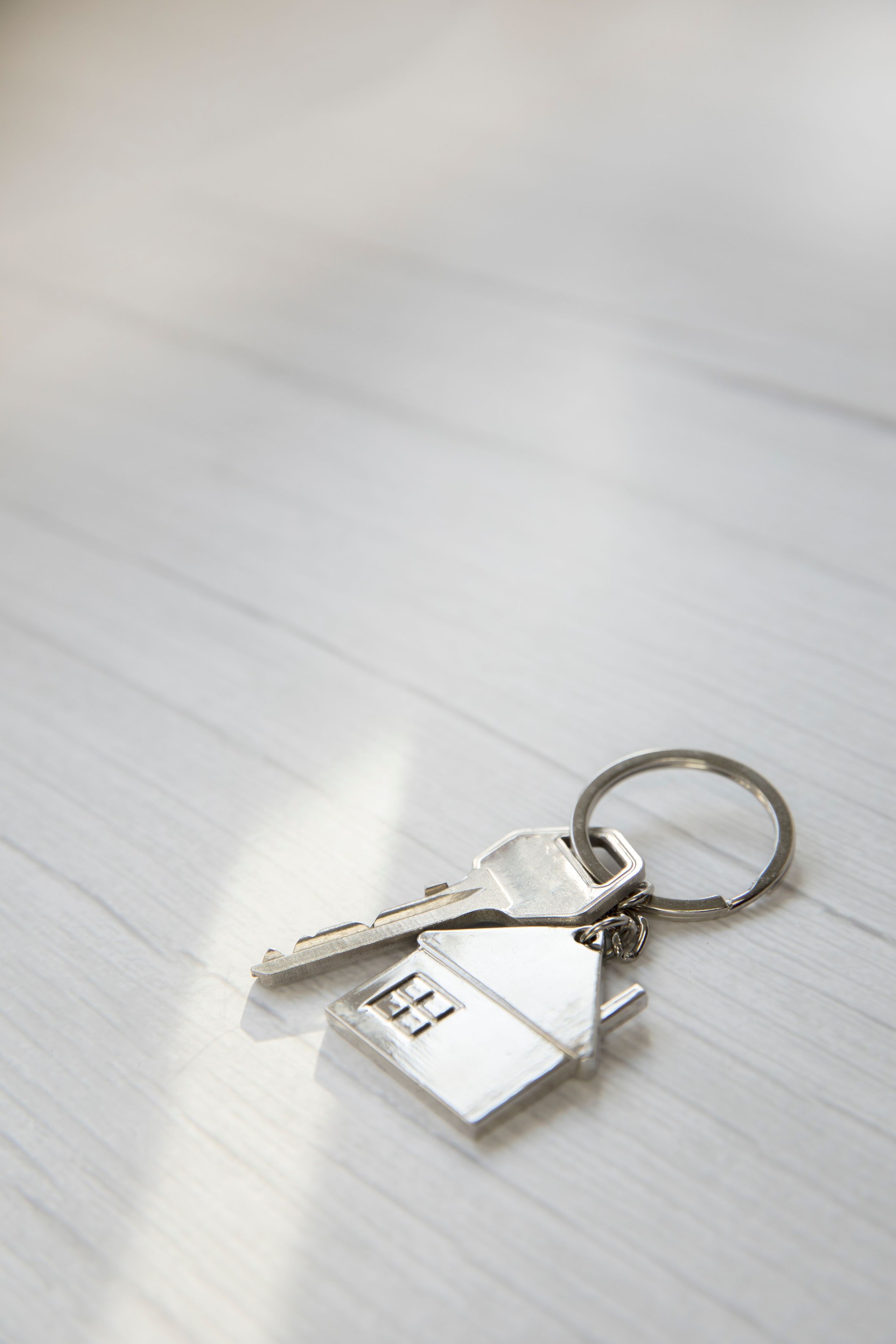 Silver key with silver house figure on white wooden background, buying new house real estate concept copy space